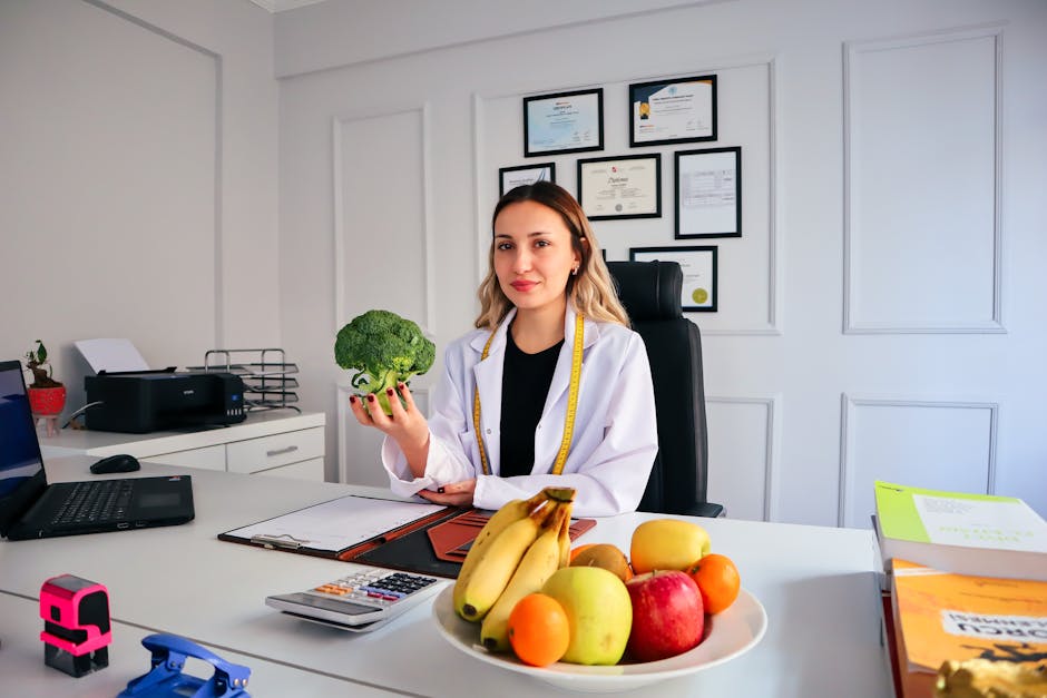 pexels-photo-15319047-15319047 Female nutritionist in office holding broccoli, surrounded by fruits, promoting healthy lifestyle.